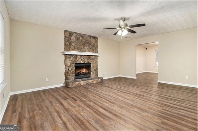 unfurnished living room with a stone fireplace, ceiling fan, dark hardwood / wood-style flooring, and a textured ceiling