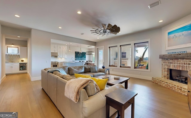 living room with ceiling fan, sink, light hardwood / wood-style floors, and a brick fireplace