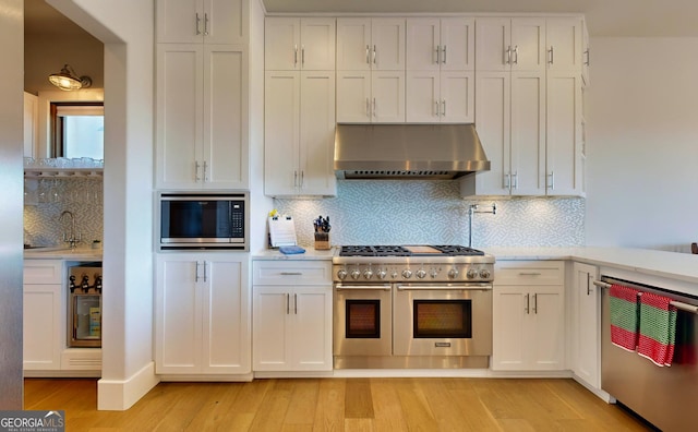 kitchen with tasteful backsplash, stainless steel appliances, range hood, and light hardwood / wood-style flooring