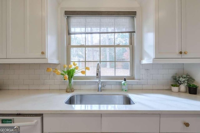 kitchen with white dishwasher, white cabinetry, sink, and tasteful backsplash