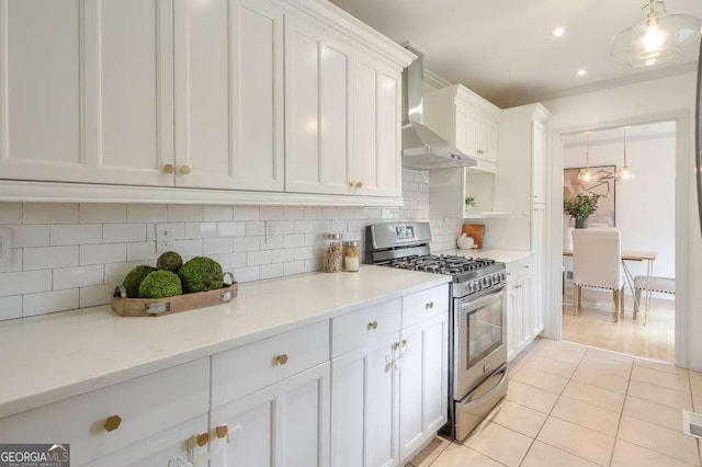 kitchen with pendant lighting, gas range, wall chimney exhaust hood, light tile patterned floors, and white cabinetry