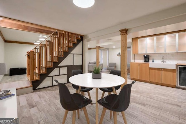 dining room with decorative columns, wine cooler, sink, and light hardwood / wood-style floors