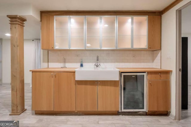 kitchen with decorative backsplash, ornate columns, sink, and beverage cooler