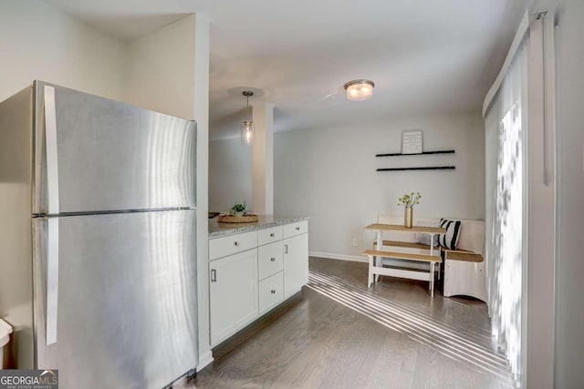 kitchen featuring light stone countertops, stainless steel fridge, dark wood-type flooring, pendant lighting, and white cabinets