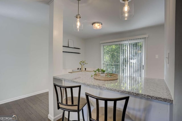 kitchen featuring a kitchen breakfast bar, decorative light fixtures, light stone counters, and dark wood-type flooring