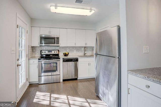 kitchen with sink, backsplash, wood-type flooring, white cabinets, and appliances with stainless steel finishes