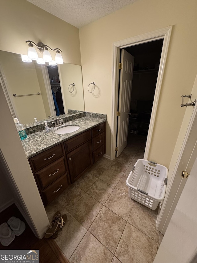 full bathroom with a walk in closet, a textured ceiling, vanity, and tile patterned flooring