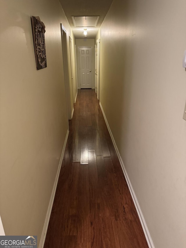 hall with baseboards, attic access, and dark wood-style floors