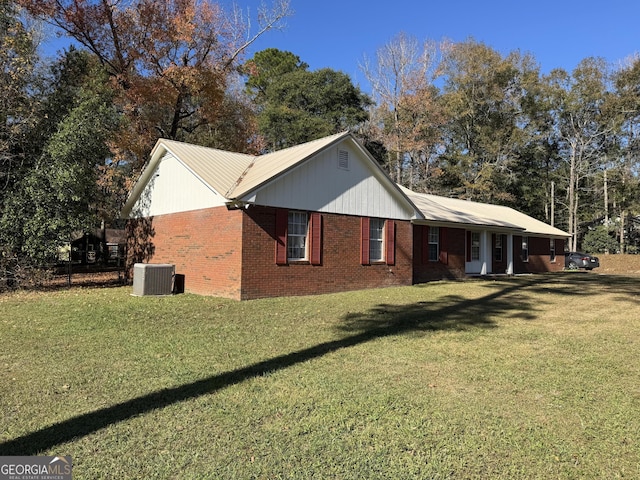 view of side of home with cooling unit, brick siding, and a lawn