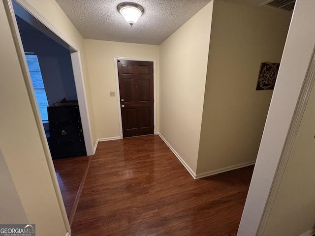 hallway featuring visible vents, baseboards, a textured ceiling, and wood finished floors