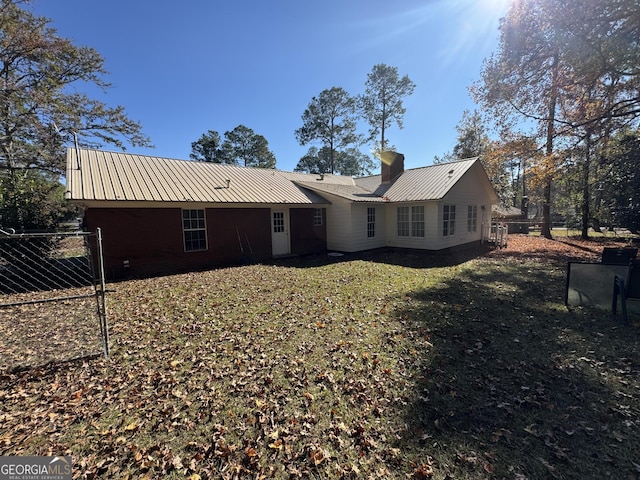 back of property featuring a chimney, a lawn, metal roof, and fence