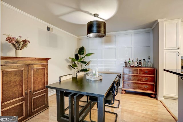 dining area featuring bar area, light hardwood / wood-style floors, and ornamental molding