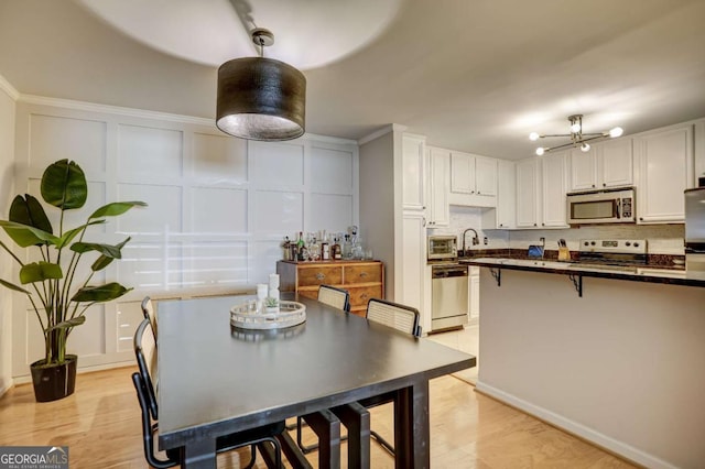 kitchen with sink, hanging light fixtures, light wood-type flooring, white cabinetry, and stainless steel appliances