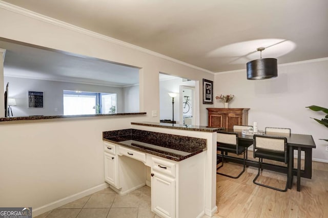 kitchen featuring hanging light fixtures, kitchen peninsula, crown molding, dark stone countertops, and white cabinets