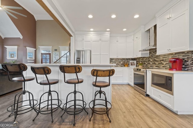 kitchen featuring wall chimney exhaust hood, a center island, white cabinetry, and stainless steel appliances