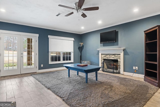 living room featuring french doors, a stone fireplace, hardwood / wood-style flooring, ceiling fan, and ornamental molding