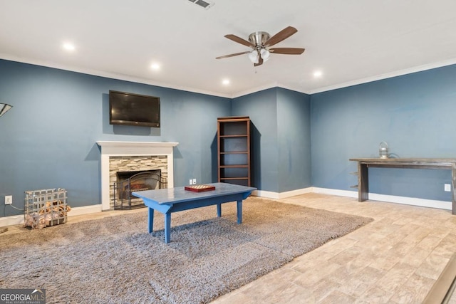 living room featuring ceiling fan, wood-type flooring, ornamental molding, and a tiled fireplace