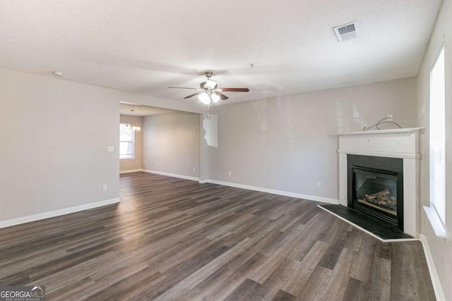 unfurnished living room featuring ceiling fan with notable chandelier, a textured ceiling, and dark wood-type flooring