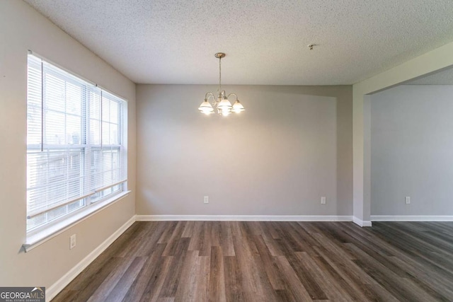 empty room with a textured ceiling, dark hardwood / wood-style flooring, and a notable chandelier