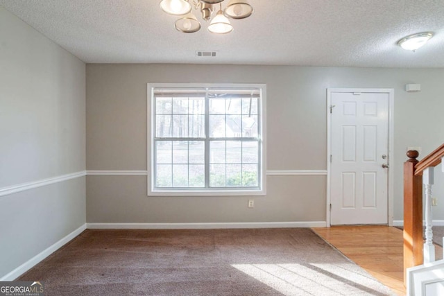 unfurnished room with a textured ceiling, light colored carpet, and an inviting chandelier