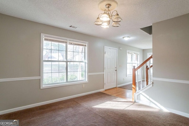 entryway with a textured ceiling, light colored carpet, plenty of natural light, and a notable chandelier