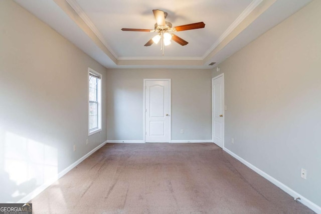 carpeted spare room featuring a raised ceiling, ceiling fan, and ornamental molding