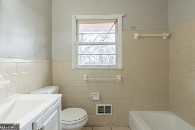 bathroom with a tub, vanity, tile walls, and toilet