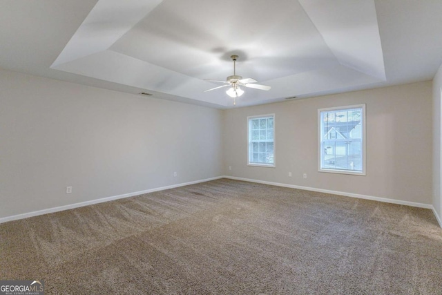 unfurnished room with a raised ceiling, ceiling fan, and carpet flooring