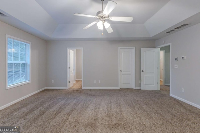 unfurnished bedroom featuring a tray ceiling, ensuite bath, ceiling fan, and light colored carpet