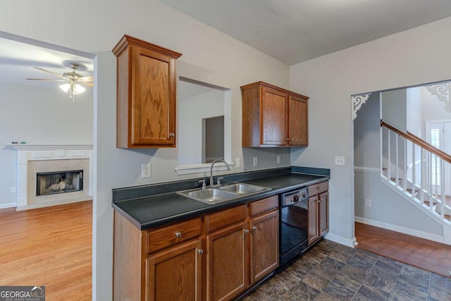 kitchen featuring ceiling fan, sink, black dishwasher, dark hardwood / wood-style floors, and a tiled fireplace