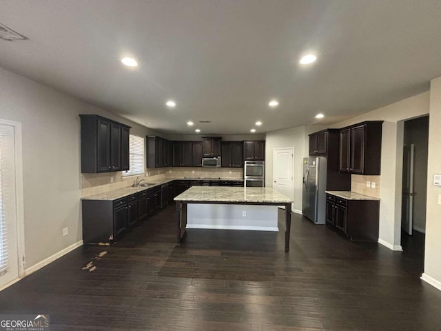 kitchen with light stone countertops, dark hardwood / wood-style flooring, stainless steel appliances, sink, and a kitchen island