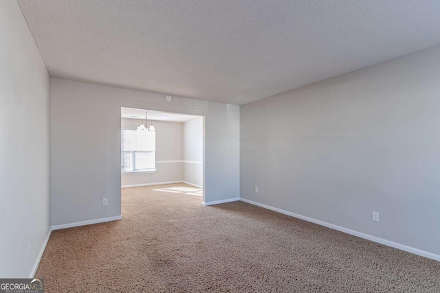 carpeted spare room featuring a textured ceiling and an inviting chandelier