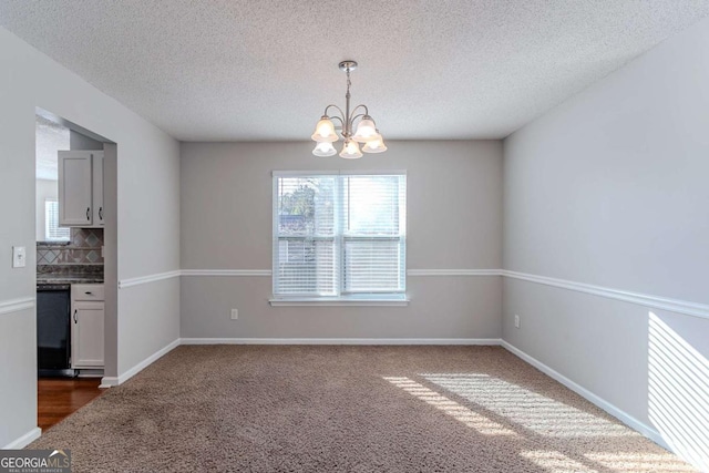 unfurnished dining area with dark colored carpet, a notable chandelier, and a textured ceiling