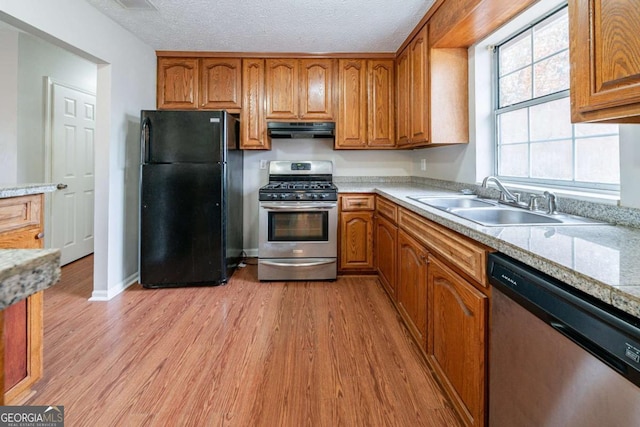 kitchen with appliances with stainless steel finishes, light stone counters, a textured ceiling, sink, and light hardwood / wood-style floors