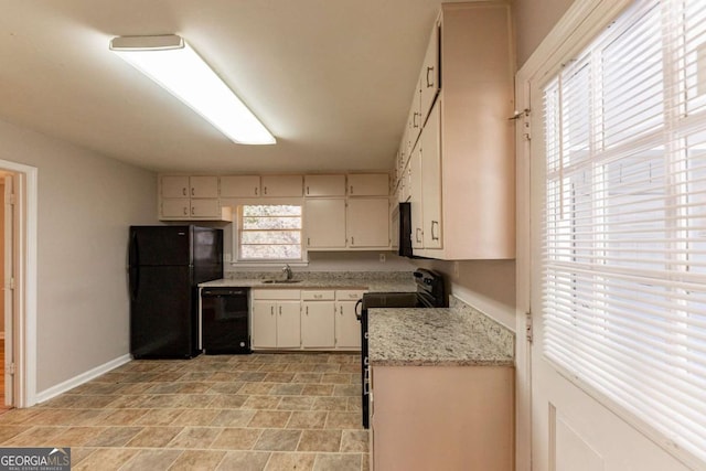 kitchen with light stone counters, sink, black appliances, and cream cabinetry