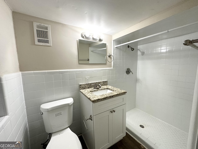 bathroom featuring toilet, a tile shower, tile walls, and vanity