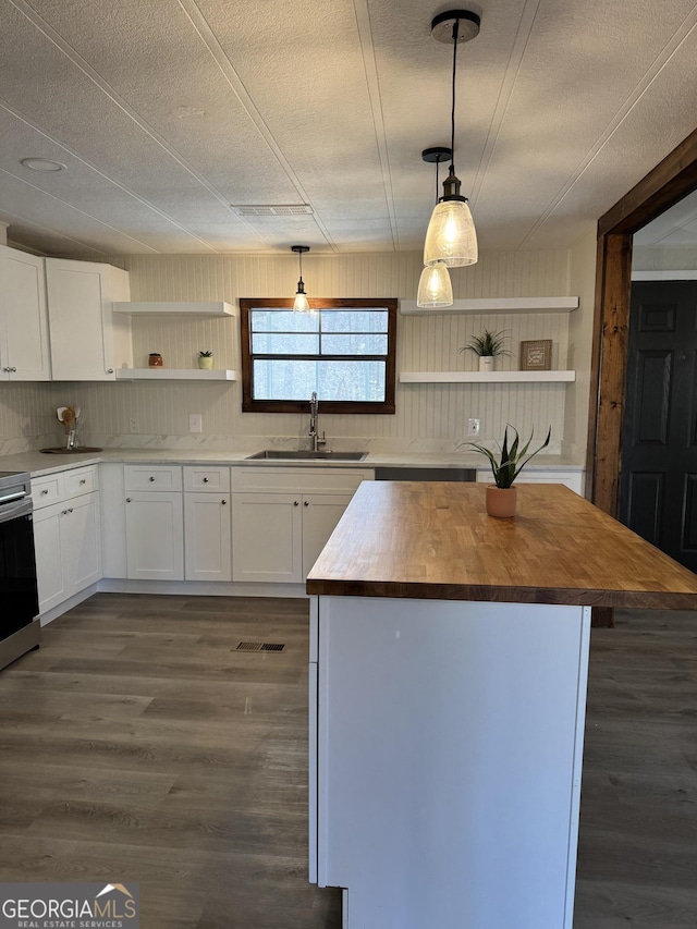 kitchen with decorative light fixtures, open shelves, wooden counters, a kitchen island, and a sink