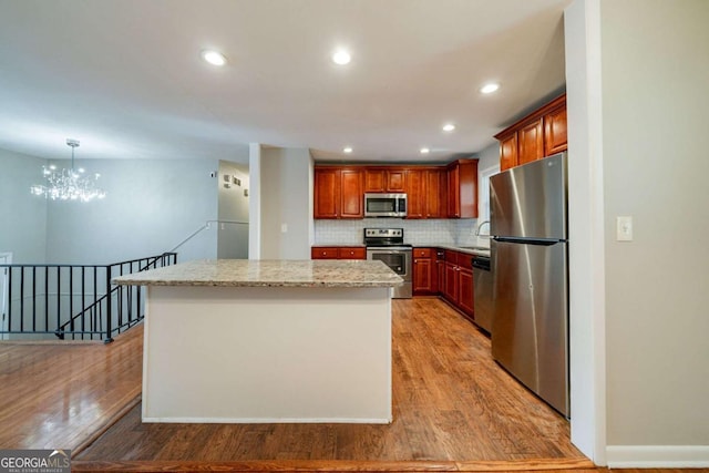 kitchen with a center island, light hardwood / wood-style flooring, a notable chandelier, light stone counters, and stainless steel appliances