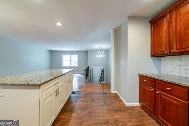 kitchen featuring decorative light fixtures, dark hardwood / wood-style floors, decorative backsplash, light stone countertops, and a notable chandelier