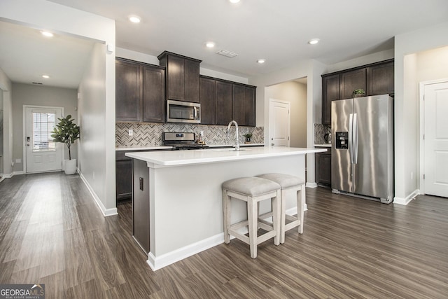 kitchen featuring a breakfast bar, dark wood-type flooring, a center island with sink, appliances with stainless steel finishes, and dark brown cabinets