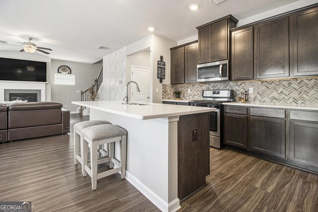 kitchen with dark wood-type flooring, sink, an island with sink, appliances with stainless steel finishes, and dark brown cabinets