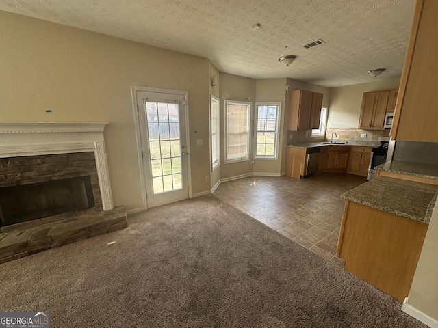 kitchen featuring stainless steel appliances, backsplash, light colored carpet, a textured ceiling, and a fireplace