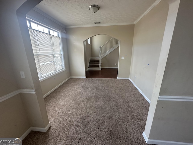 spare room with a textured ceiling, dark carpet, and crown molding