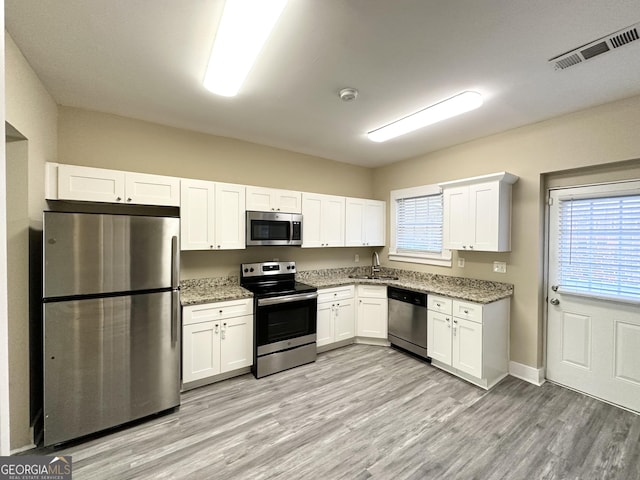 kitchen with sink, light hardwood / wood-style flooring, light stone countertops, appliances with stainless steel finishes, and white cabinetry