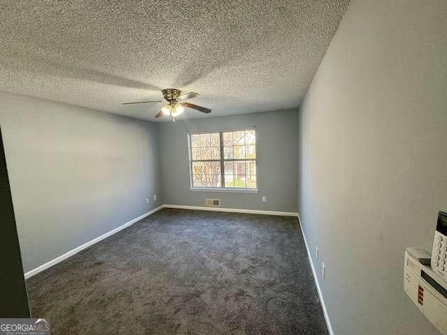 empty room featuring ceiling fan, dark carpet, and a textured ceiling