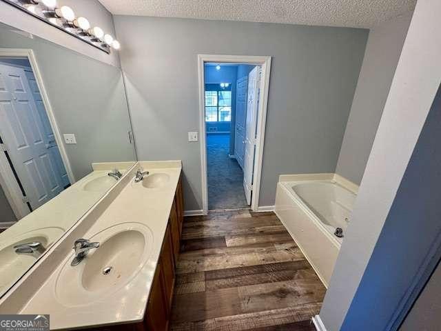 bathroom featuring vanity, a textured ceiling, hardwood / wood-style flooring, and a tub