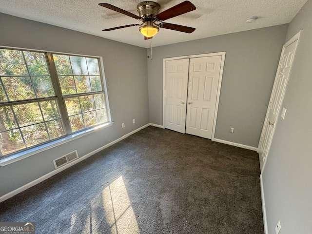 unfurnished bedroom featuring dark colored carpet, ceiling fan, a textured ceiling, and a closet