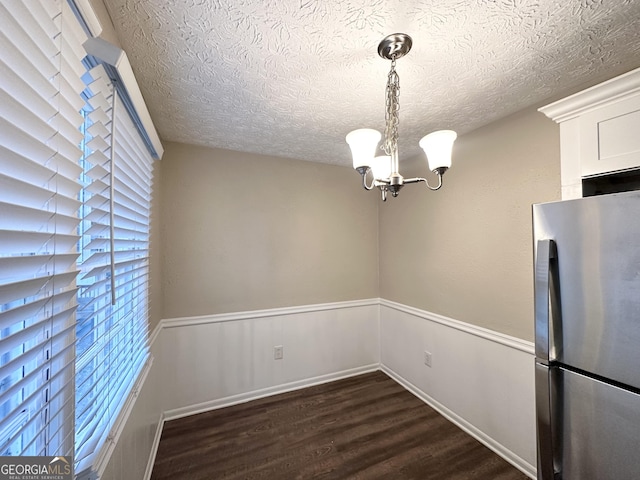 unfurnished dining area featuring dark hardwood / wood-style flooring, a chandelier, and a textured ceiling