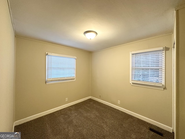 empty room featuring dark carpet, ornamental molding, and a wealth of natural light