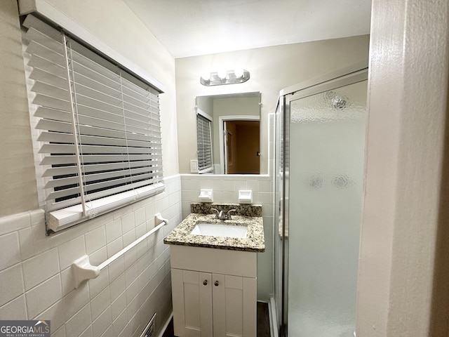 bathroom with vanity, a shower with door, and tile walls